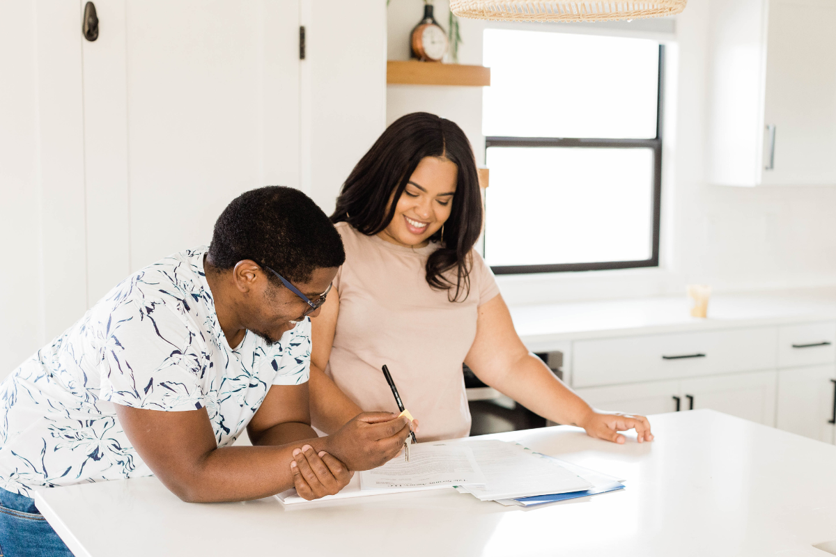 a female and male couple standing at a kitchen counter with paperwork and smiles